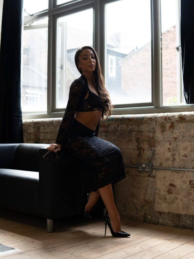 Woman in black lace outfit by window.