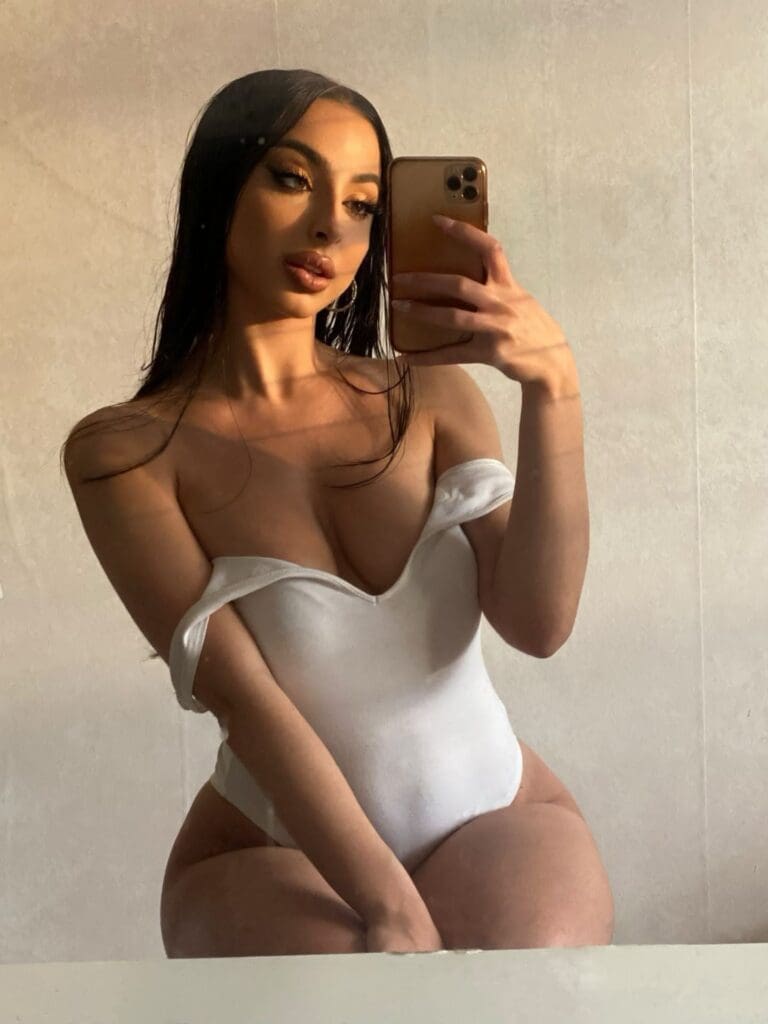 Woman taking mirror selfie in white outfit.