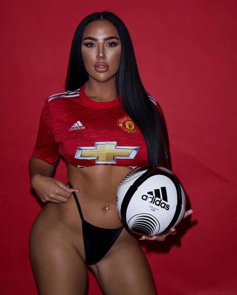 Woman in Manchester United jersey holding soccer ball.