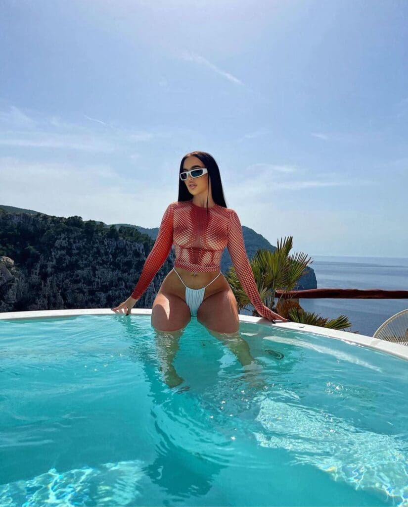 Woman posing in pool, wearing sunglasses.