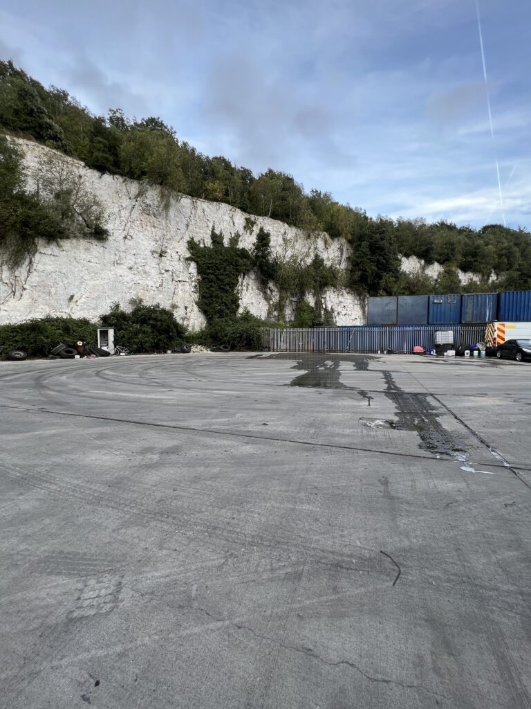 Industrial yard with containers and cliff background.