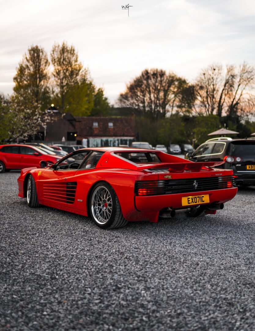 Red sports car parked on gravel lot.
