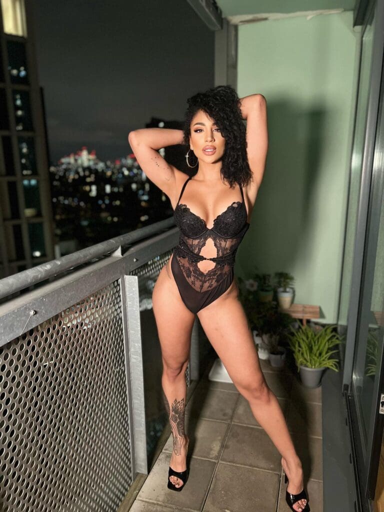 Woman posing on balcony in black lingerie.