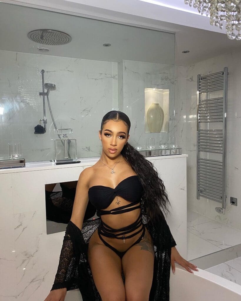 Woman in black bikini sitting in bathroom.