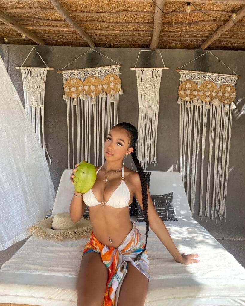 Woman in bikini holding coconut, sitting indoors.