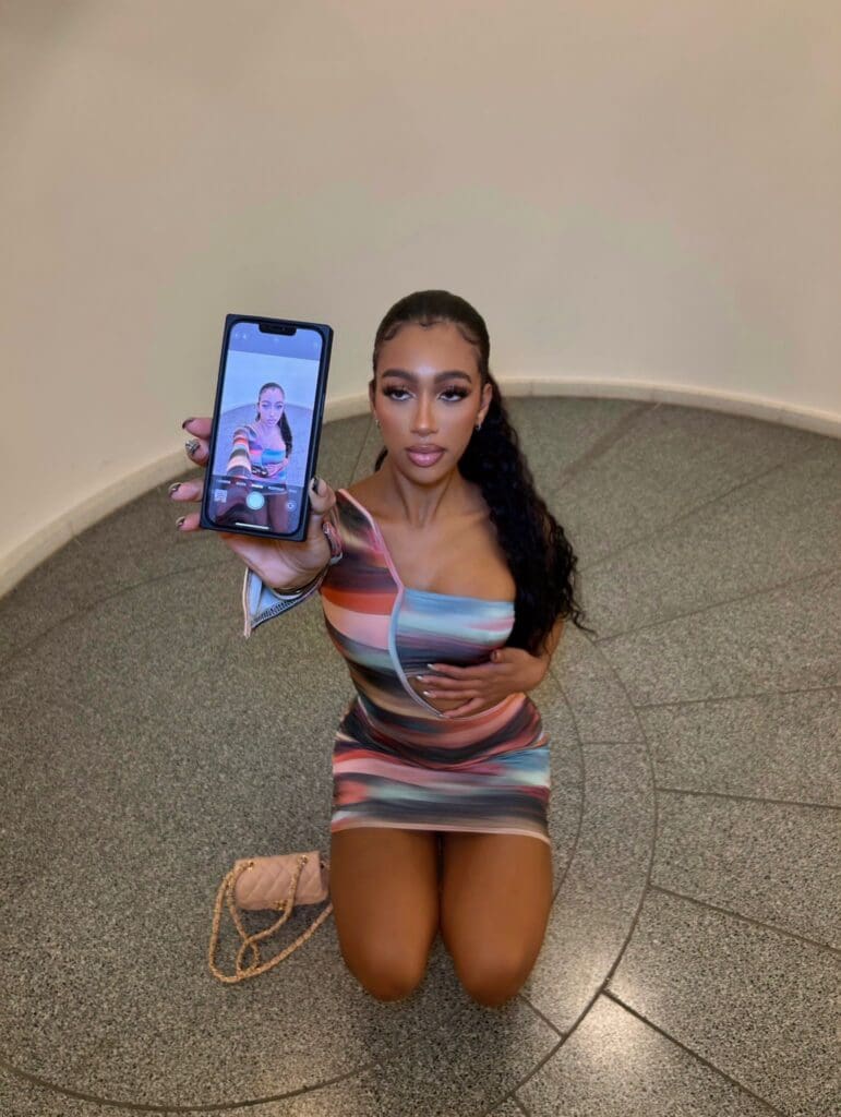 Woman kneeling, holding phone displaying selfie.