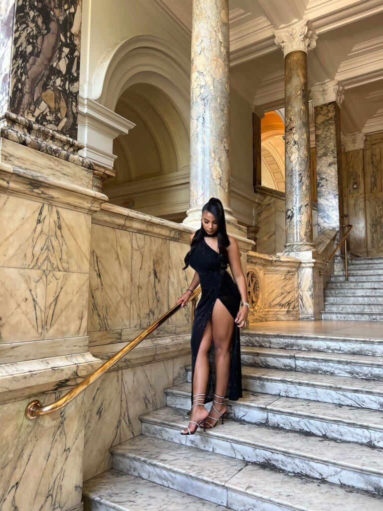 Woman descending elegant marble staircase in gown.