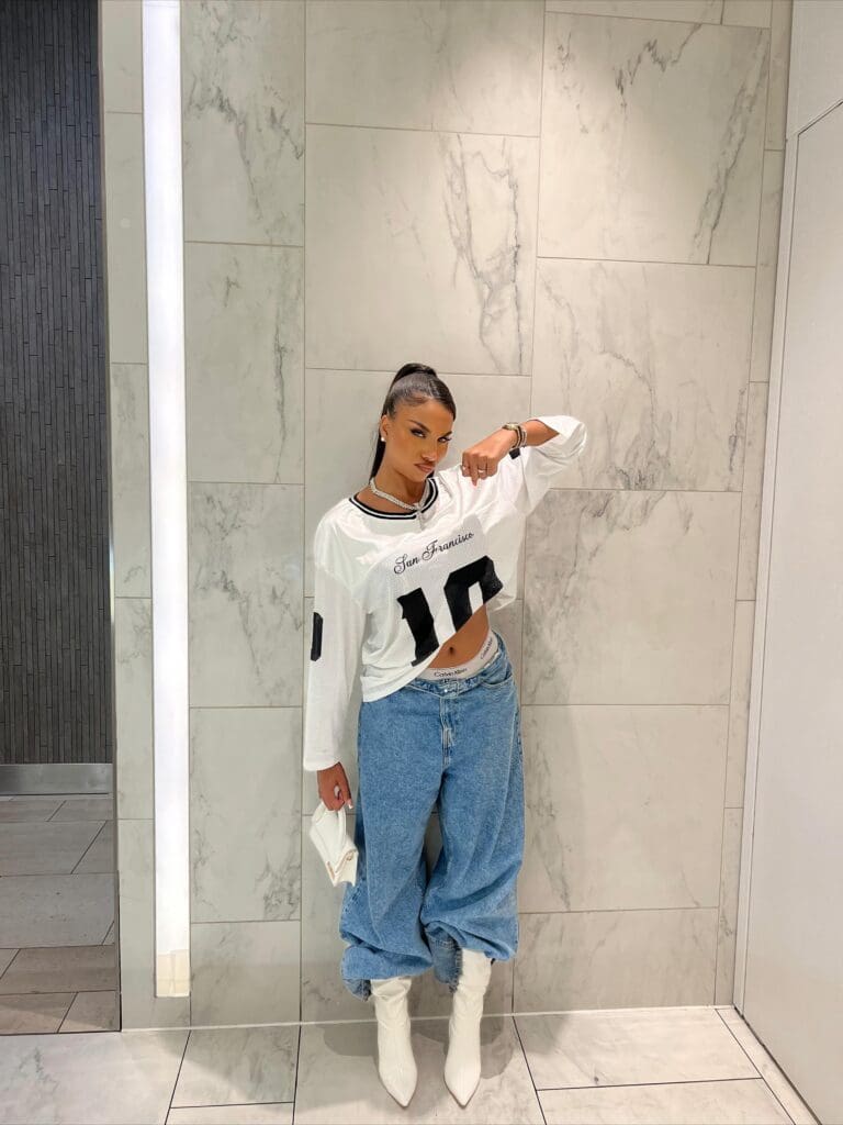 Woman in casual outfit posing against wall.